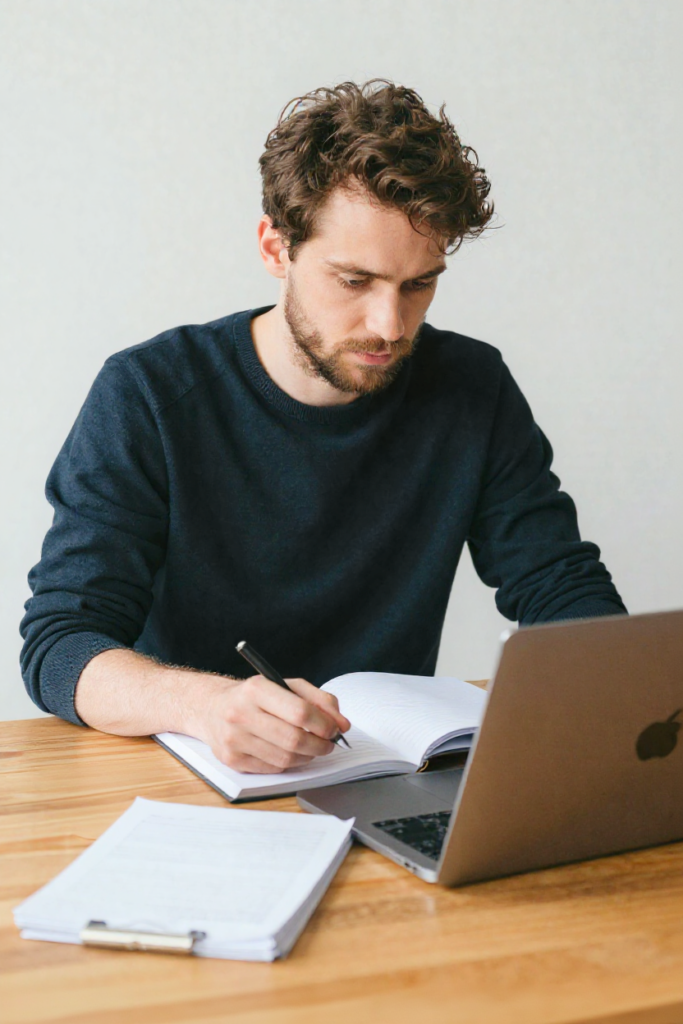 man die een online ondernemer is, zittend aan laptop met notities